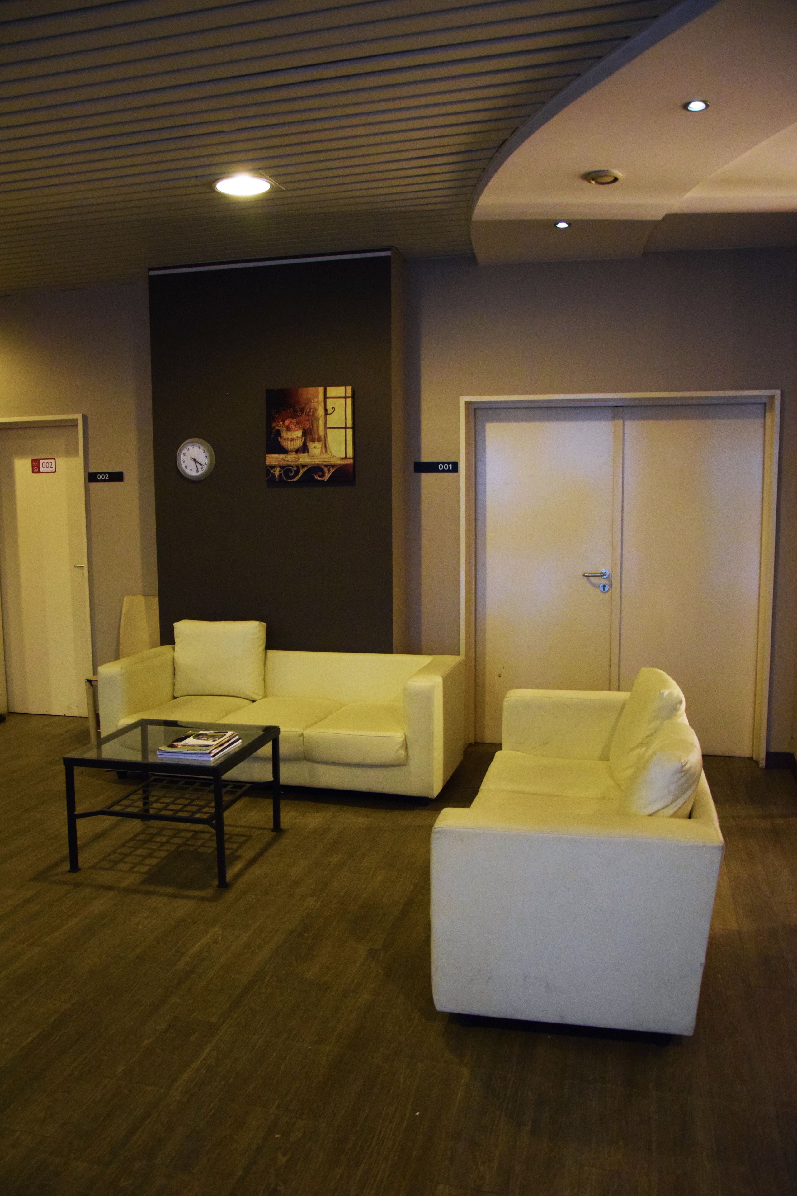 Eine Hotelhalle mit einer Rezeption, zwei Sofas, einer Uhr und einer Tür mit einem Nummernschild.