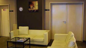 A hotel lobby with a reception desk, two sofas, a clock, and a door with a number sign.