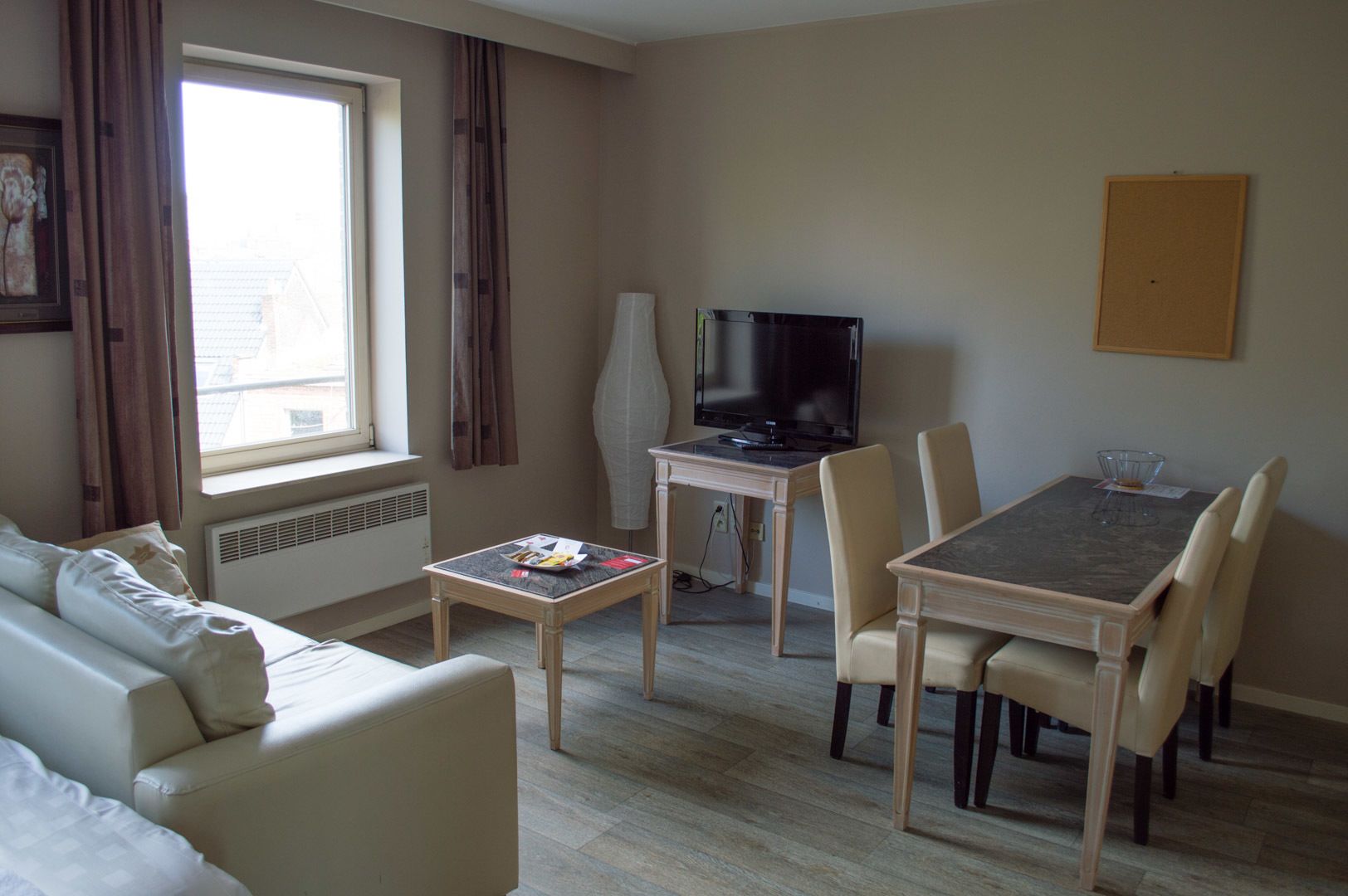 A modern living room with a sofa, a dining table with chairs, a TV, and a window with curtains.
