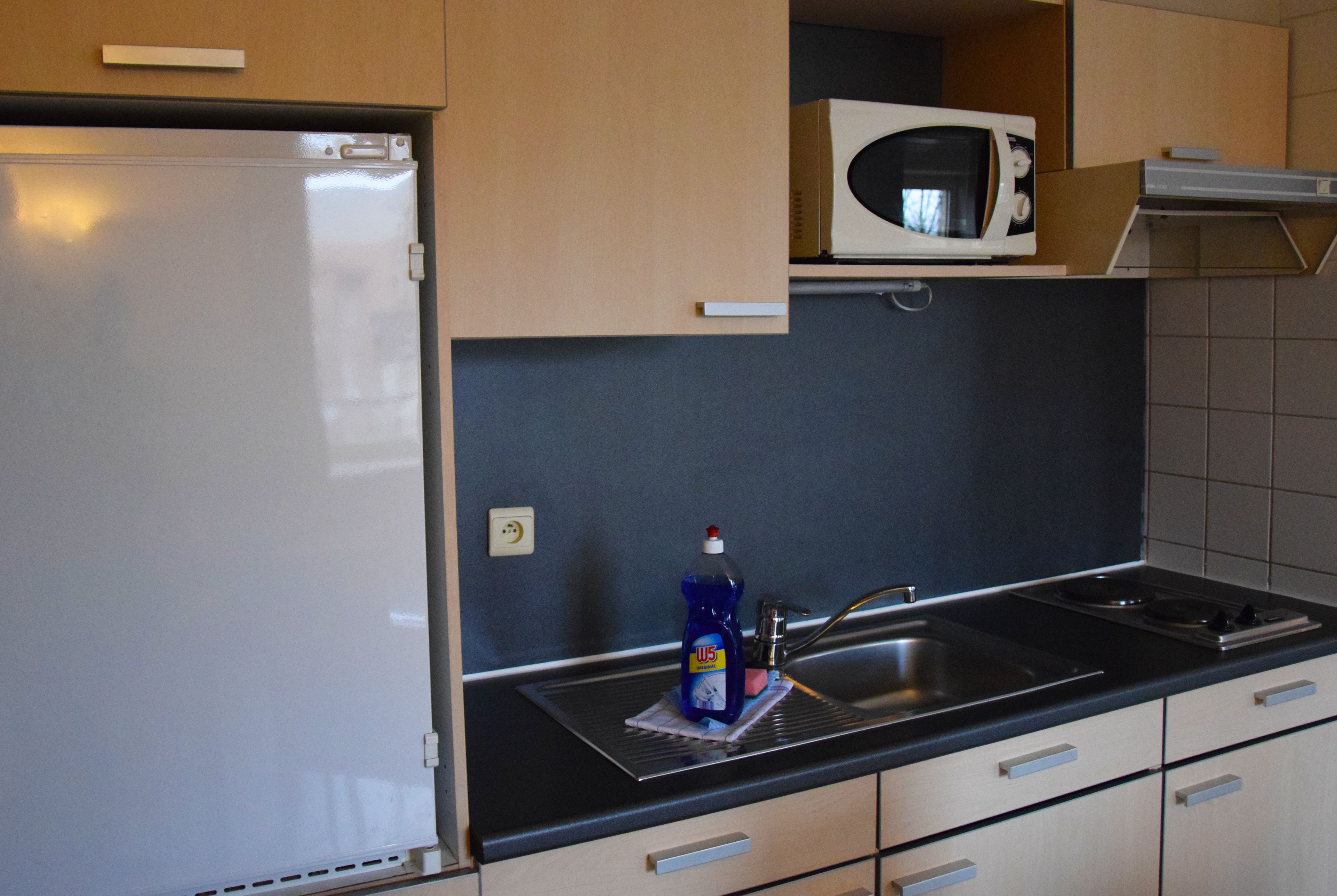 A kitchen with a refrigerator, microwave, sink, and cabinets.