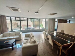 Een moderne kamer met een bank, een eettafel met stoelen en grote ramen met uitzicht op het omliggende landschap.