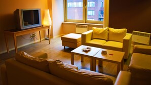 Een woonkamer met een bank, een salontafel, een televisie op een standaard en een lamp.