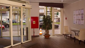 Un hall de hotel con mostrador de recepción, una planta en maceta y una puerta de vidrio que da al exterior.