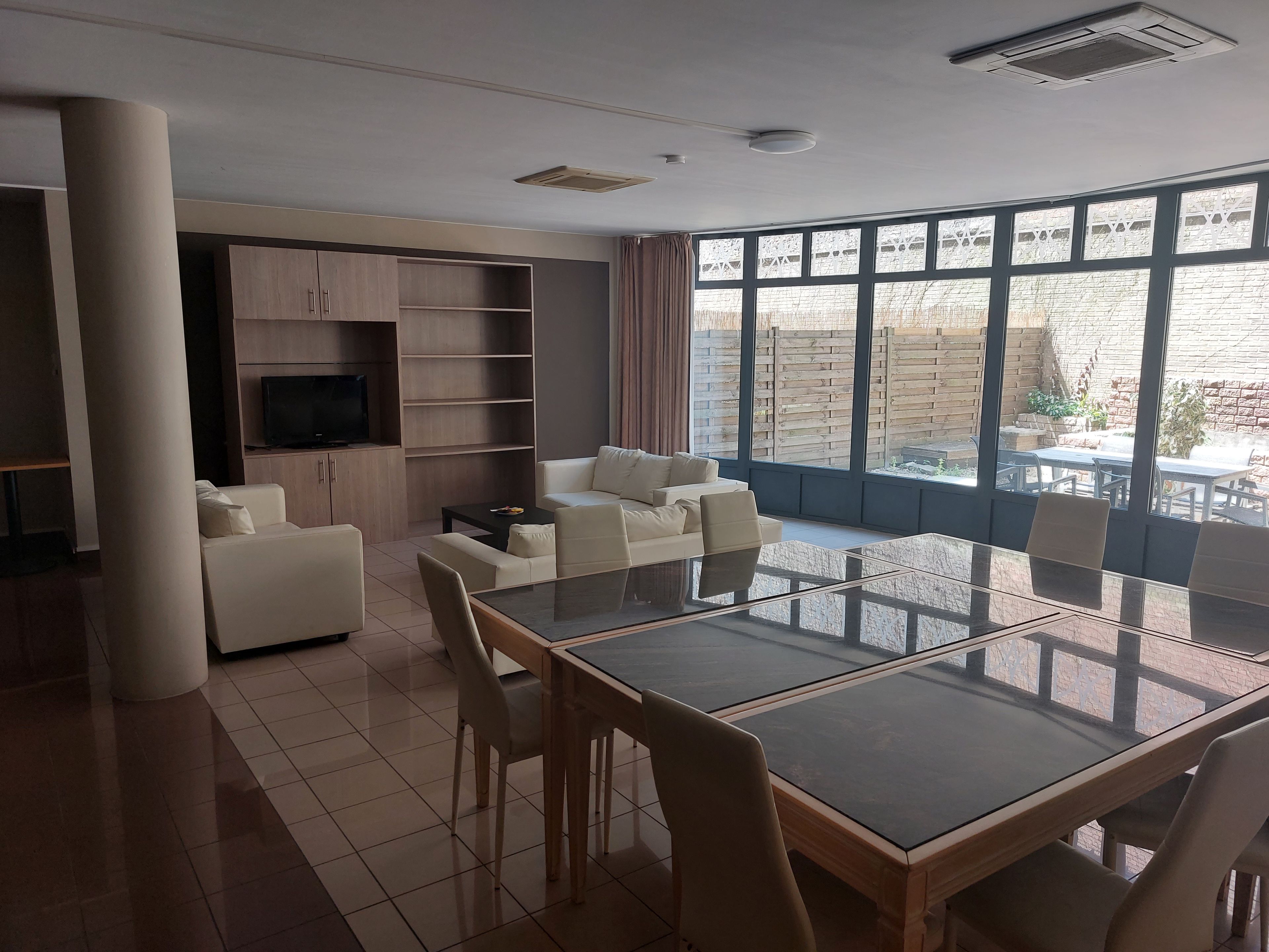 A modern living room with a glass-top dining table, white sofas, and a TV on a wooden cabinet.