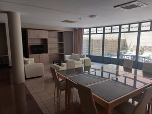 Een moderne woonkamer met een eettafel met glazen blad, witte banken en een televisie op een houten kast.
