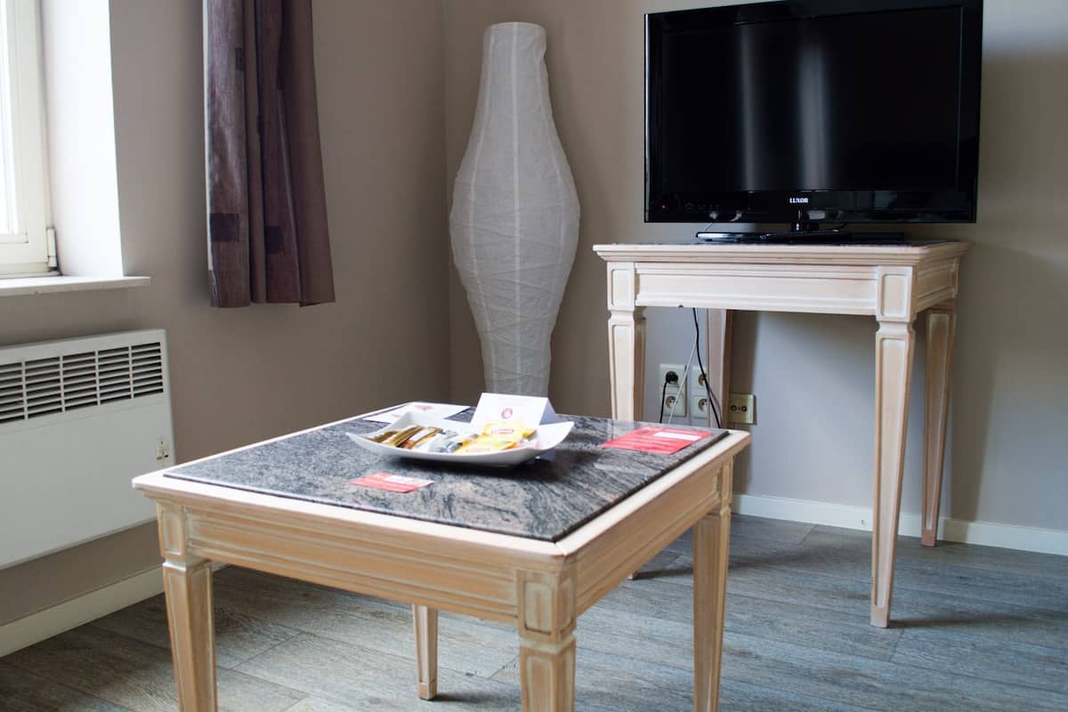 A hotel room with a wooden table, a vase, a television, and a window.