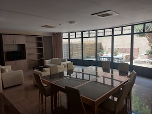 Una sala de estar moderna con una mesa de comedor de vidrio, sofás, un televisor y vistas al exterior.