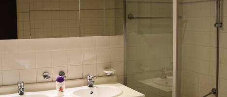 A modern bathroom with two sinks, a glass-enclosed shower, and a large mirror.