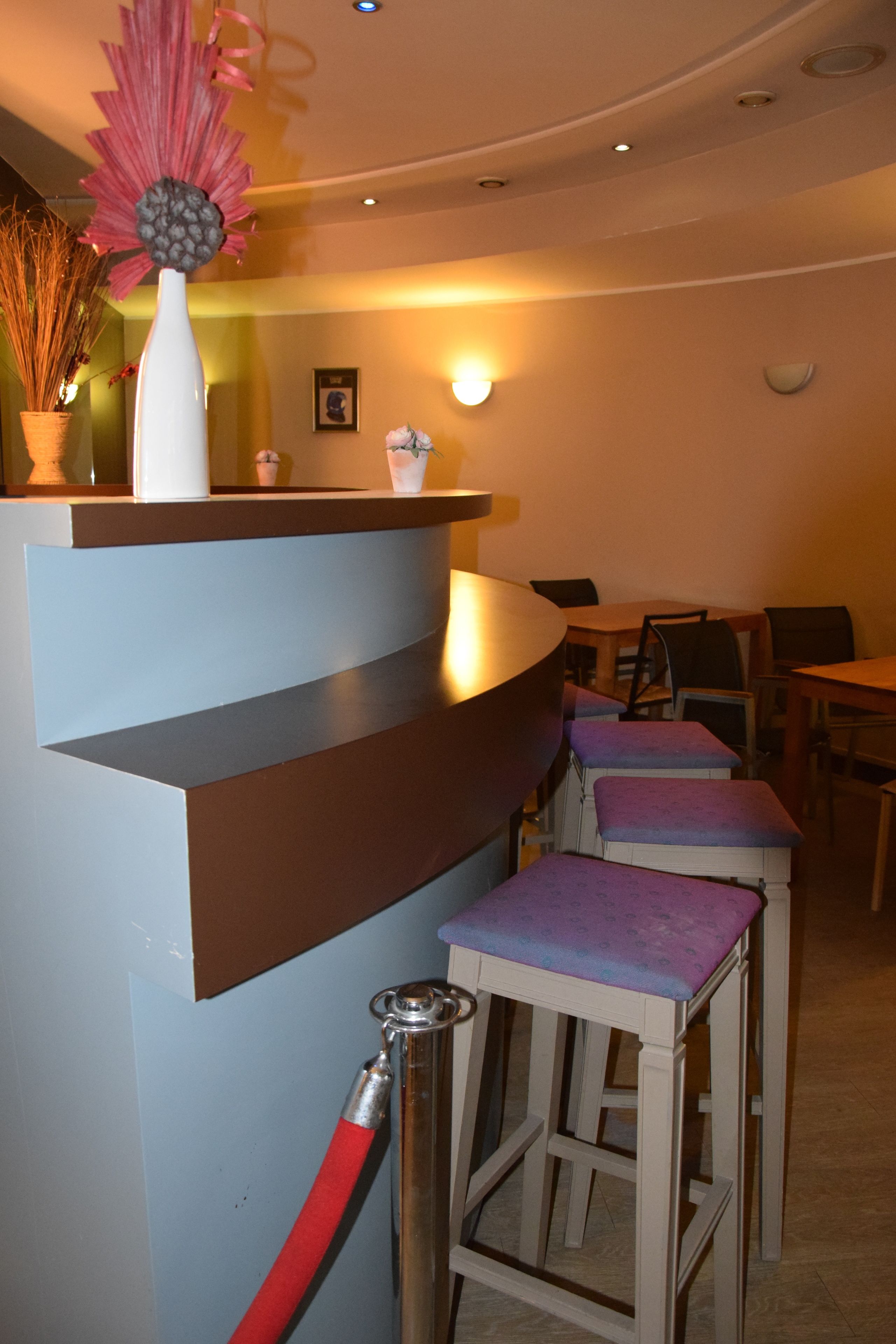 A bar area with a curved counter, bar stools, and a decorative flower arrangement.