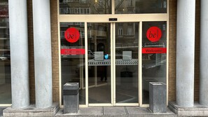 A hotel entrance with a glass door, two columns, and a 'be HOUSING' sign. - Ambassador Suites Antwerp (Antwerp)