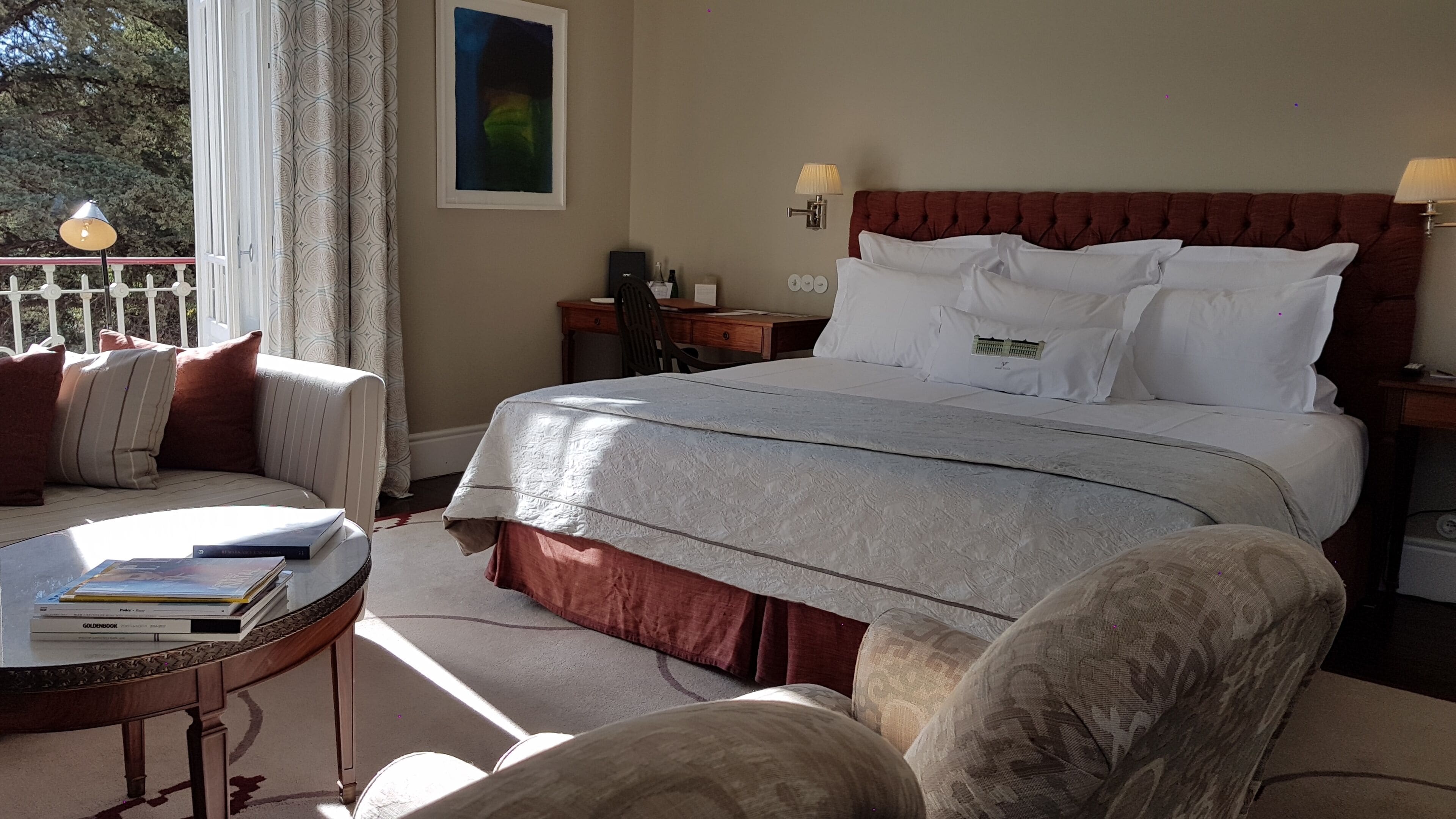Habitación de hotel con una cama grande, un escritorio, una silla y un sofá. Hay una ventana con cortinas, un cuadro en la pared y una lámpara en la mesita de noche.