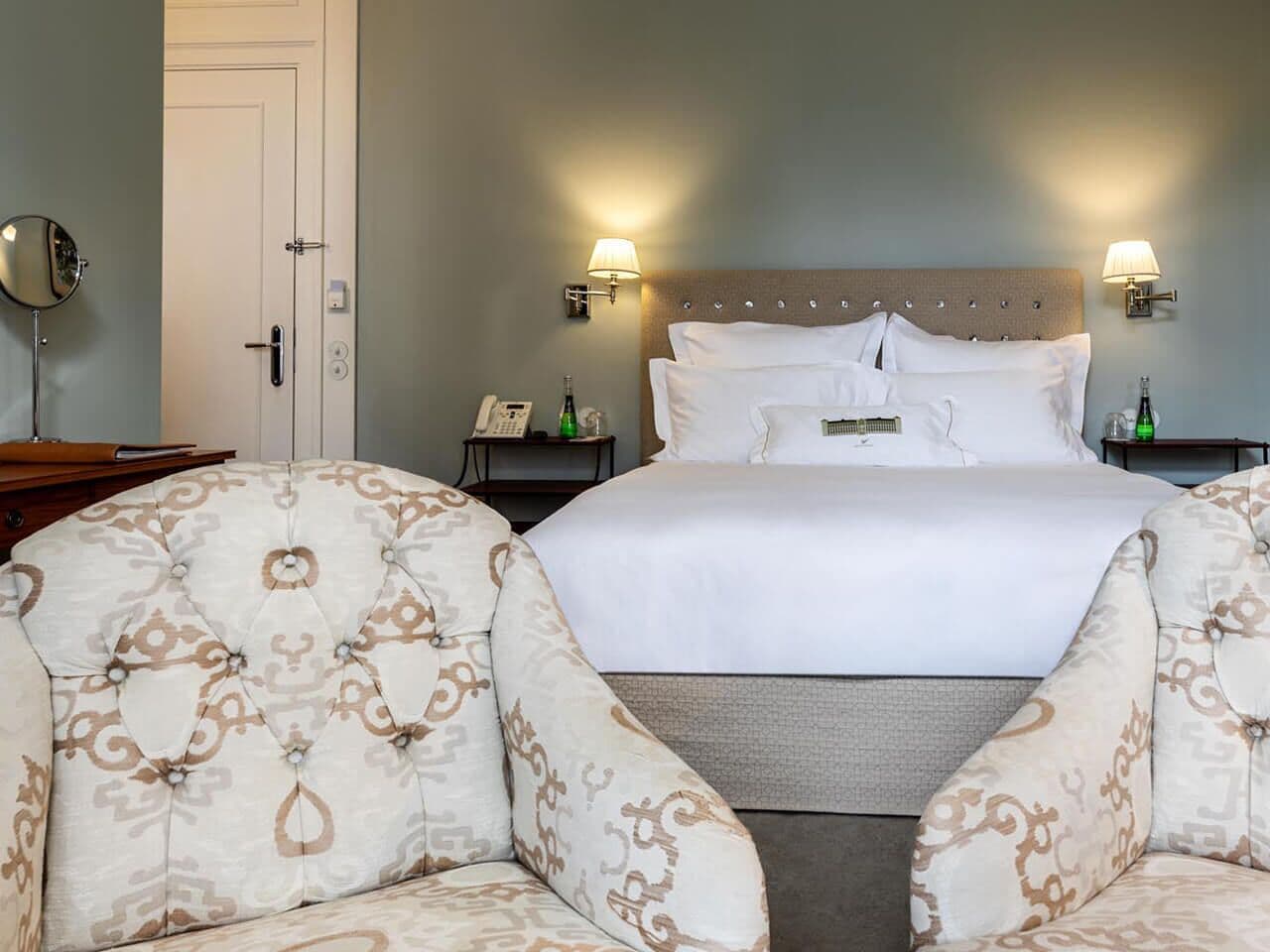 Una habitación de hotel con una cama grande, dos mesitas de noche, un revistero, una silla y un espejo.