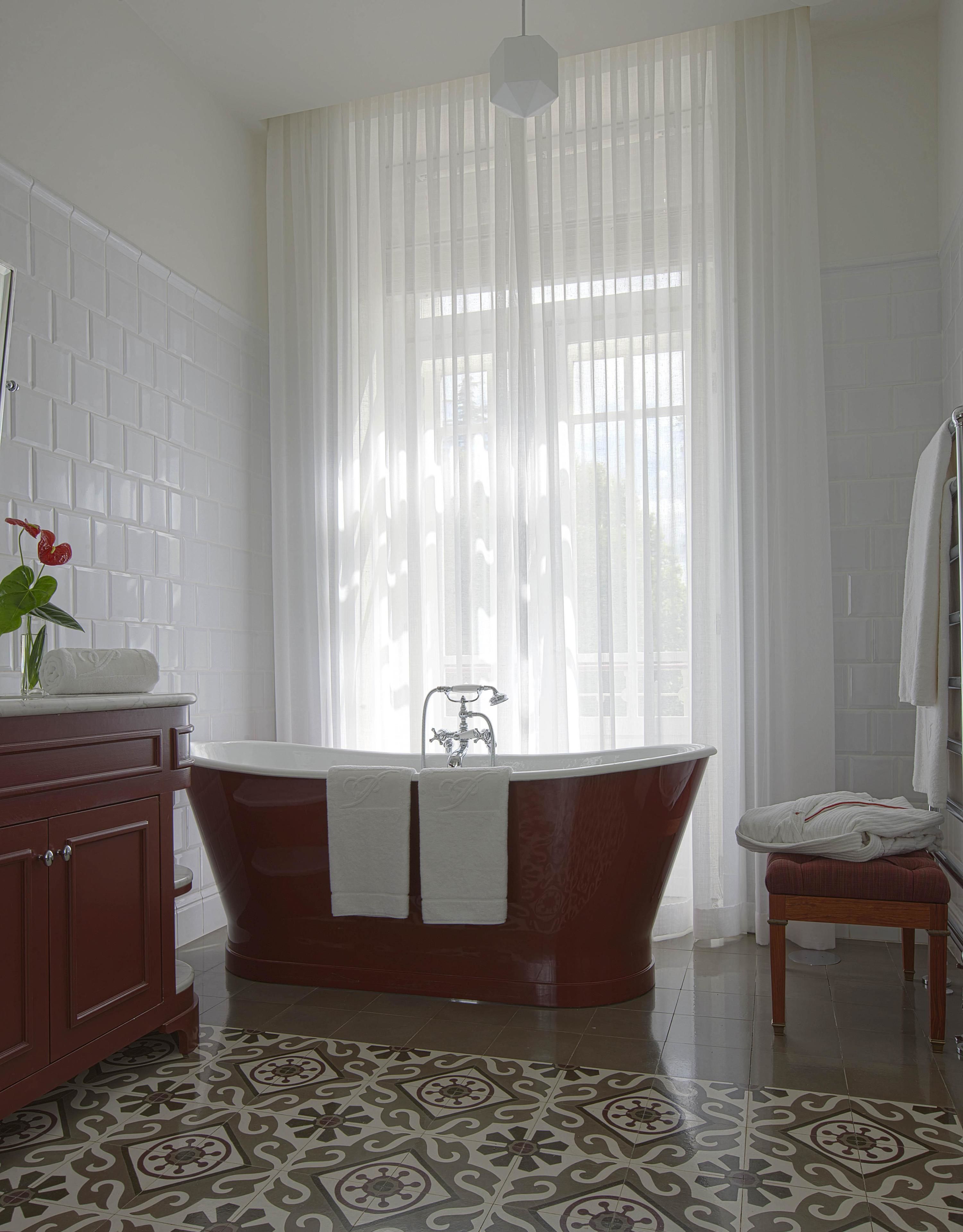 Un baño con una bañera independiente, un banco de madera, un lavabo de mármol y baldosas de suelo estampadas.