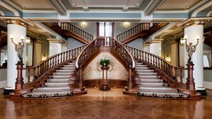 Un'imponente scalinata con ringhiere e colonne decorate, che conduce a un piano superiore.