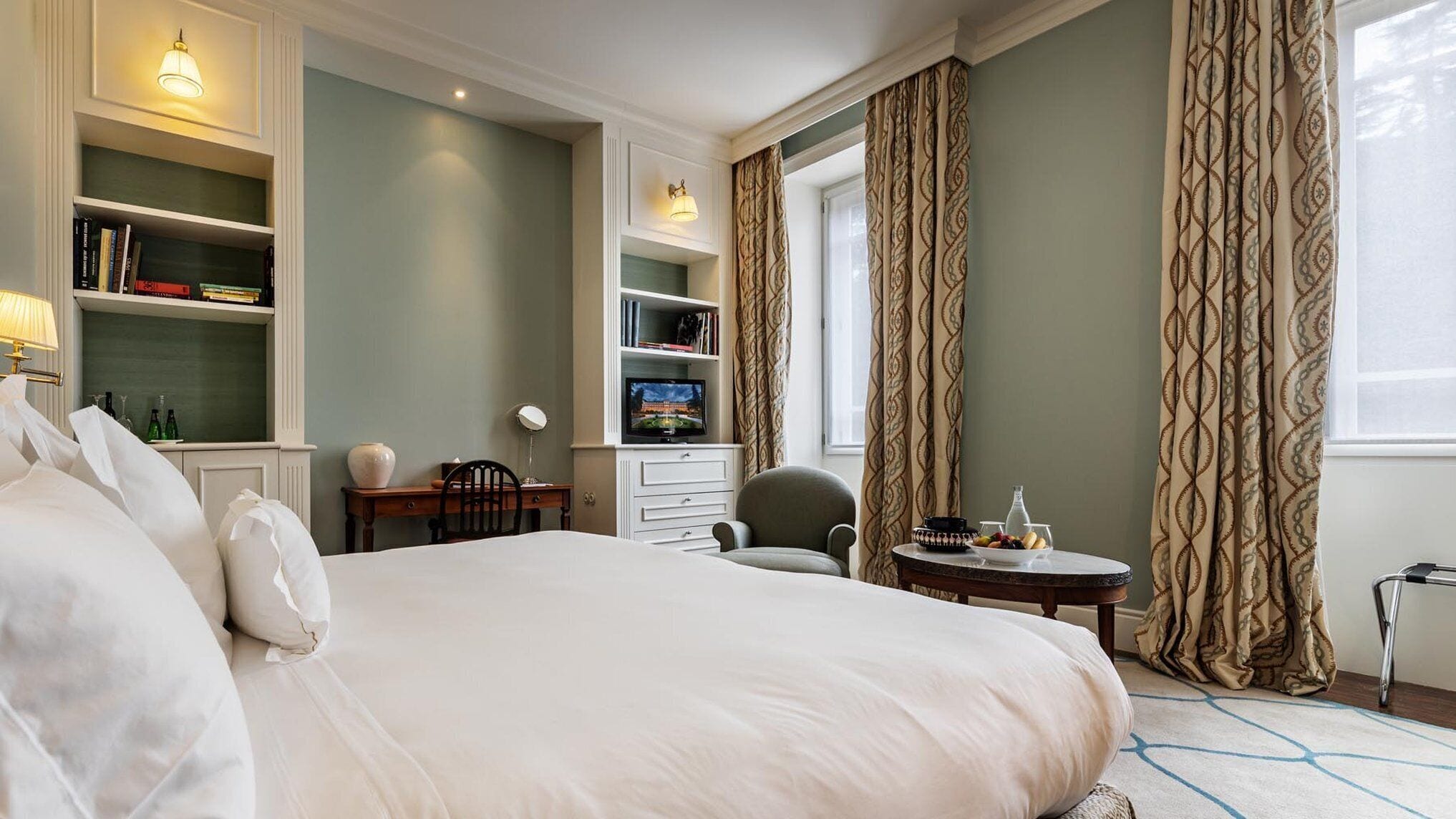 Habitación de hotel con una cama grande, un escritorio con una silla, una mesita con un florero y un televisor en un estante.
