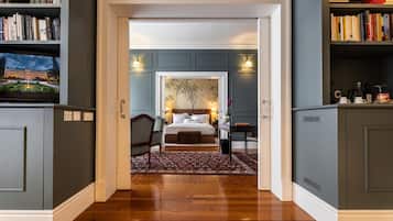 Un pasillo que conduce a un dormitorio con una cama, una mesita de noche y una silla. Hay estanterías a ambos lados del pasillo.