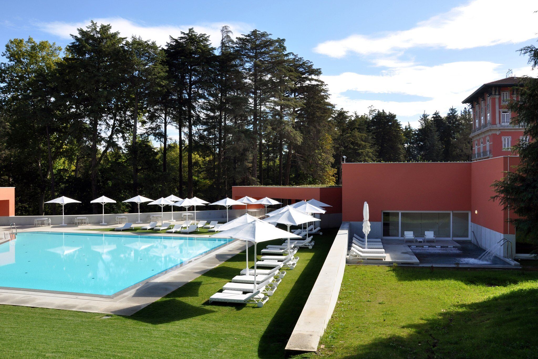 A swimming pool with lounge chairs and umbrellas, surrounded by a well-maintained lawn and tall trees.