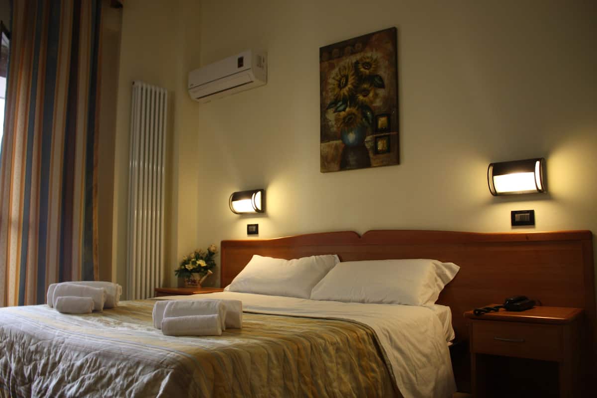 A hotel room with a neatly made bed, a nightstand with a lamp, and a painting on the wall.