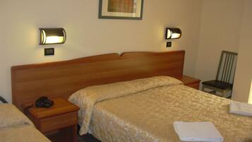 A hotel room with a wooden headboard, two bedside tables, a bed with a beige quilt, a chair, and two wall-mounted lamps.