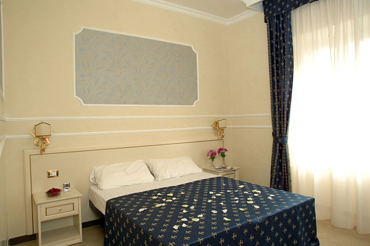 A hotel room with a bed, nightstand, lamp, and curtains.