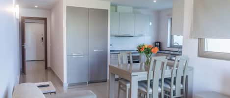 A modern living room with a sofa and a dining table with chairs. There is a kitchen area visible in the background with cabinets and a window.