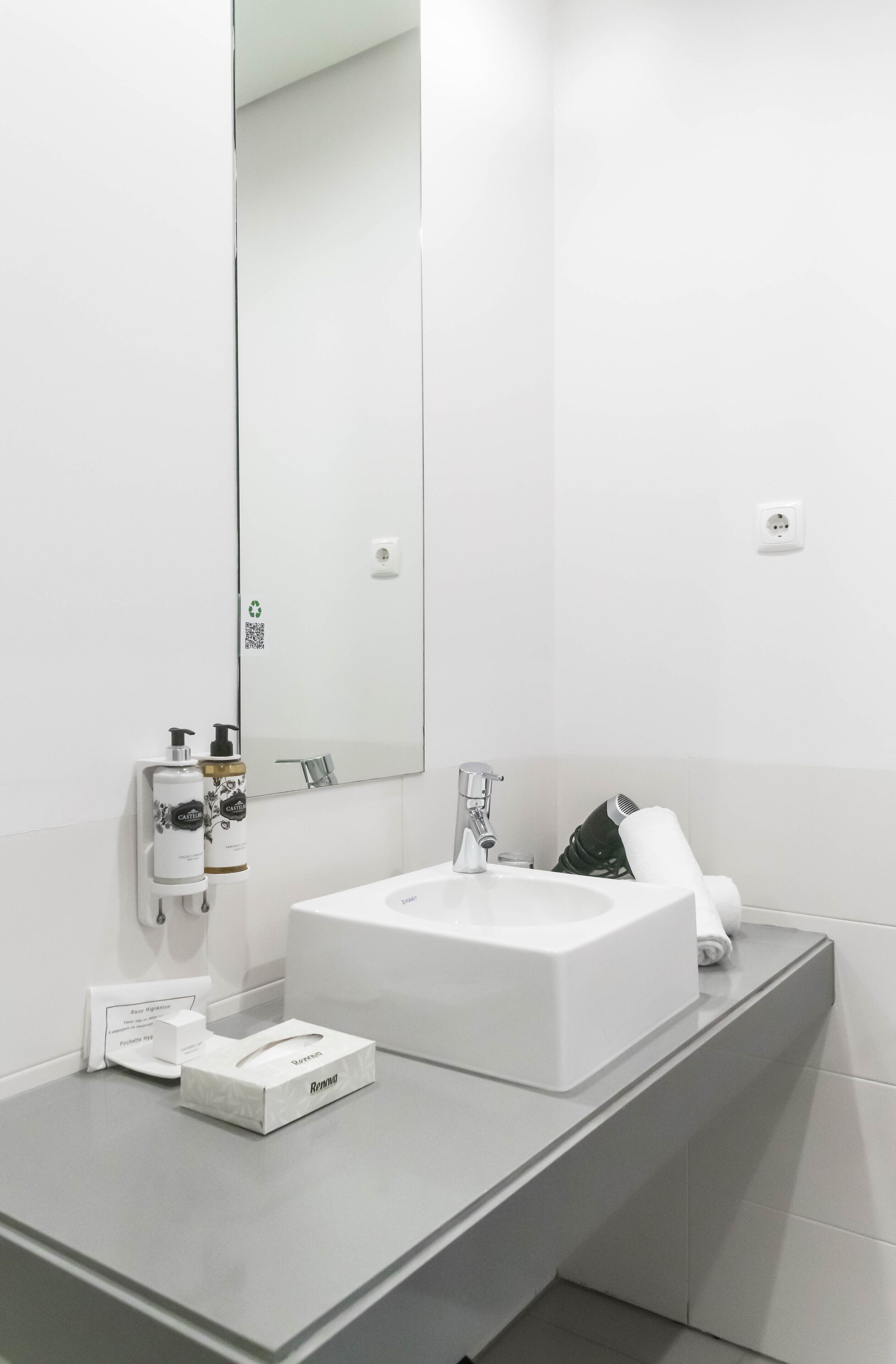 Une salle de bain moderne avec un lavabo blanc, un miroir et un distributeur de serviettes.