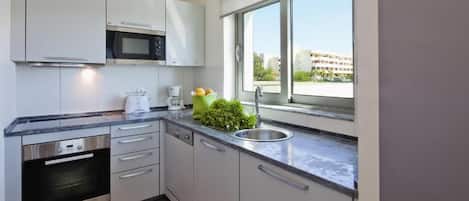 Una cuina moderna amb electrodomèstics d'acer inoxidable, una finestra amb vista a edificis i un taulell amb una cafetera i una planta.