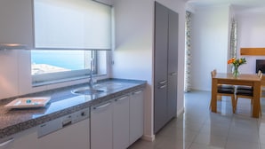 A modern kitchen with a built-in dishwasher, a window with a view of the sea, and a dining area with a table and chairs. - Villa Doris Suites (Lagos)