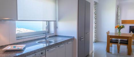 Una cocina moderna con lavavajillas incorporado, una ventana con vistas al mar y un comedor con mesa y sillas.