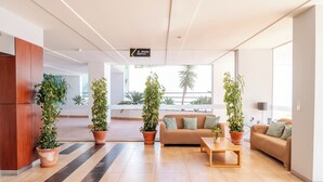 A modern hotel lobby with a sofa, coffee table, and potted plants. A sign indicates a pool area. - Villa Doris Suites (Lagos)