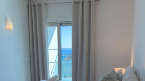 A bedroom with a bed, a bedside lamp, a view of the sea through a window, and a balcony. - Villa Doris Suites (Lagos)