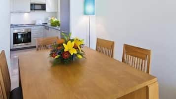 A dining area with a wooden table and chairs, a vase of flowers, and a modern kitchen in the background.