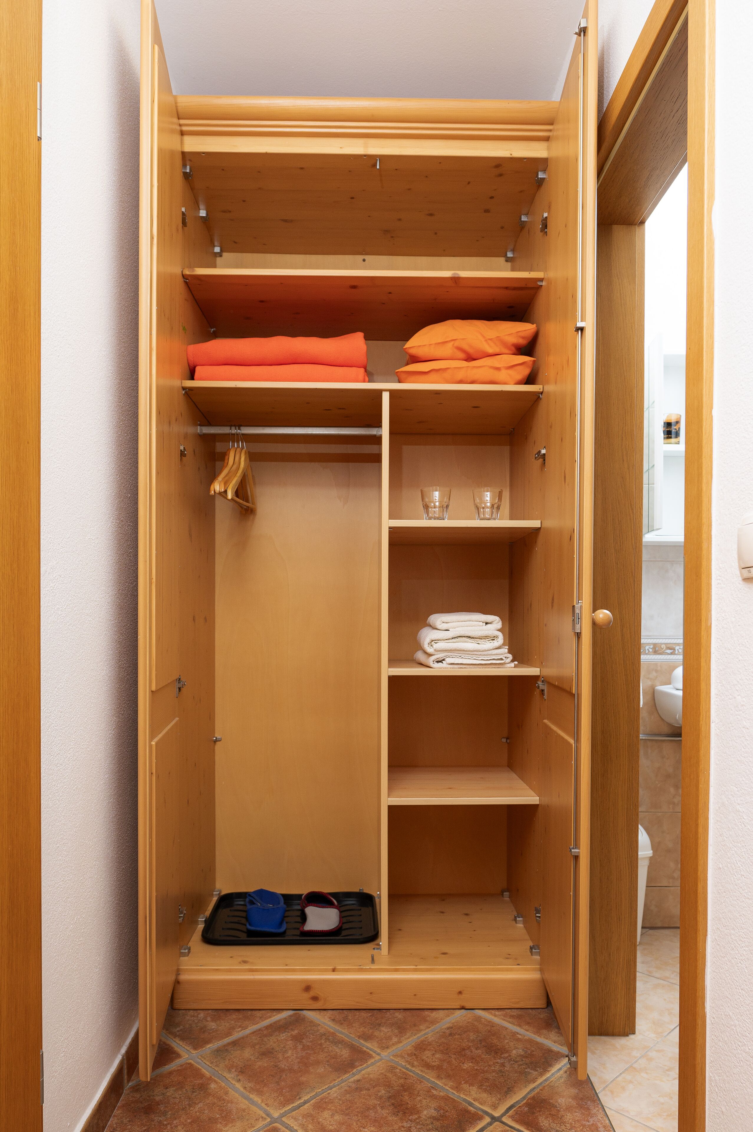 A wooden closet with shelves, a hanging rod, and a shoe rack.