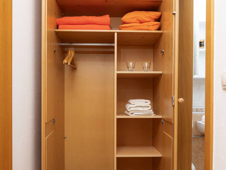 A wooden closet with shelves, a hanging rod, and a shoe rack.