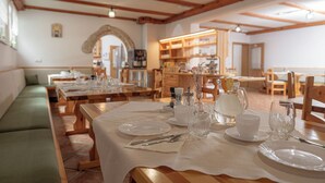 A dining area with wooden tables set for a meal, a green sofa, and a kitchen in the background. - Rooms & Apartments Pr Matjon (Bled)