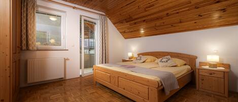 A bedroom with a wooden bed, bedside tables with lamps, a radiator, and a sliding glass door leading to a balcony.