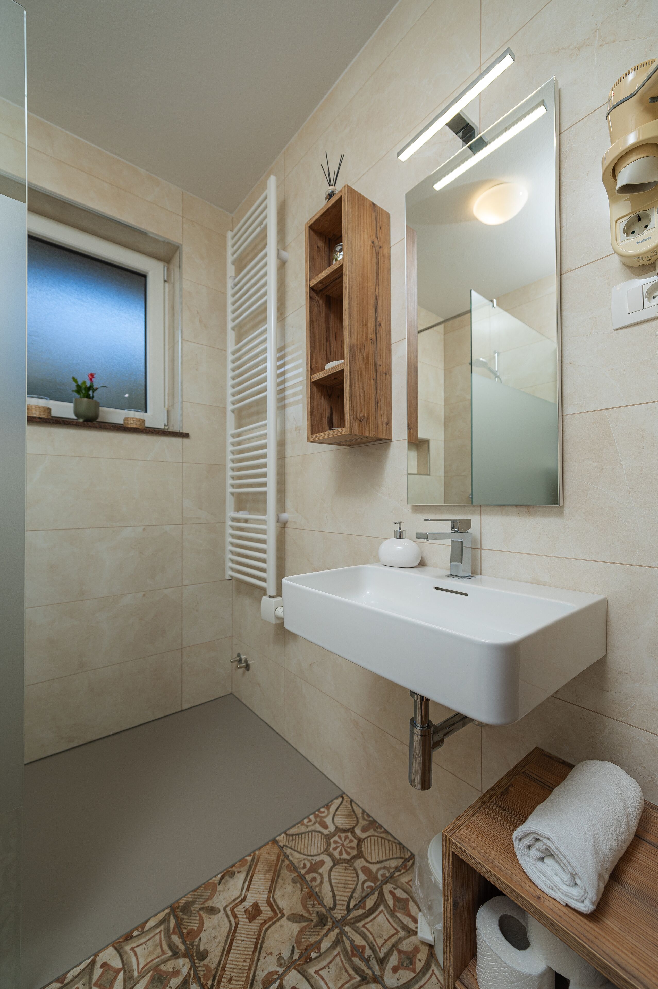 A bathroom with a white sink, a mirror, a window with a view, a towel rack, and a toilet paper holder.