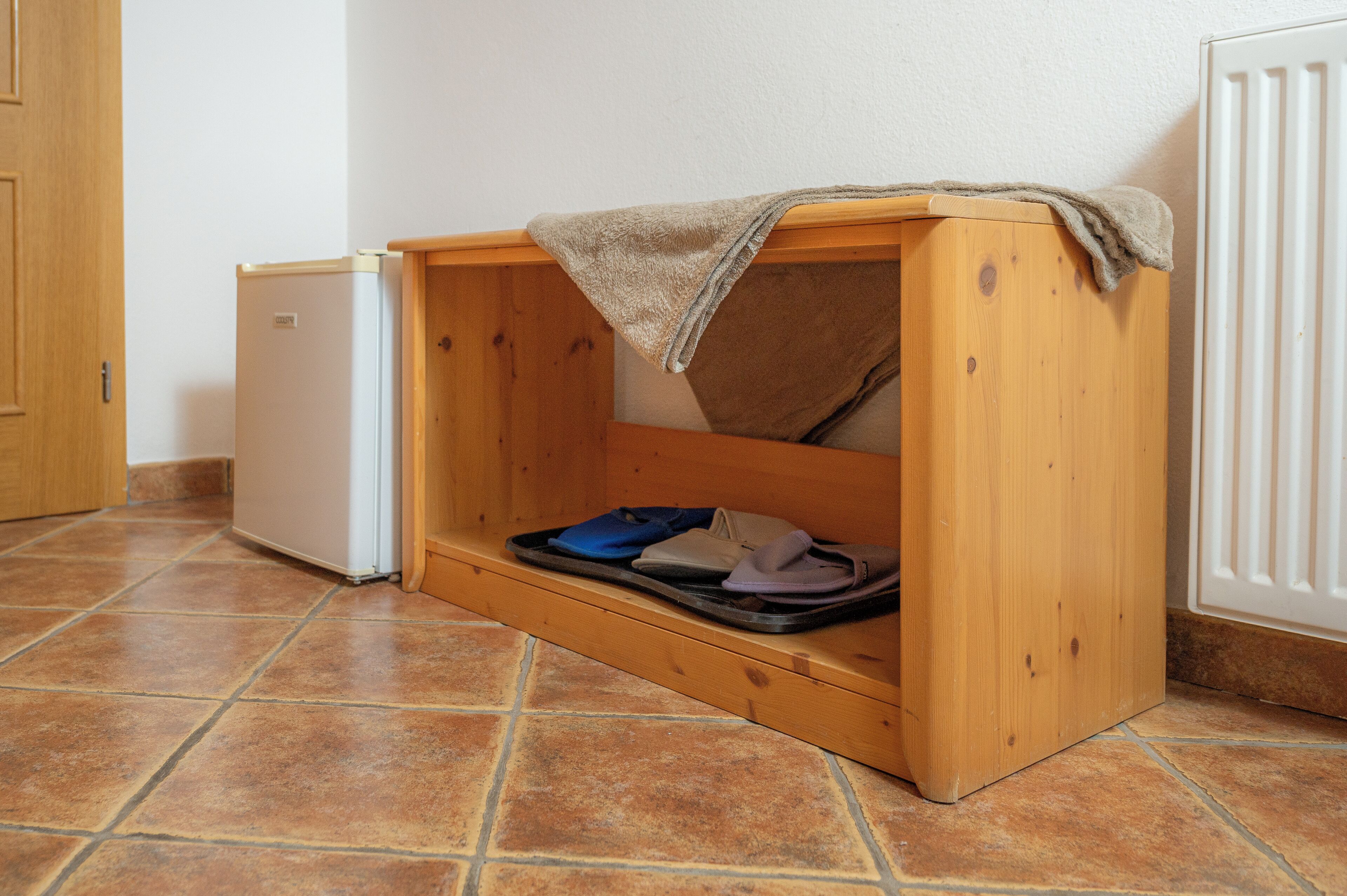 A small wooden cabinet with a towel on top, a small refrigerator, and a tiled floor.