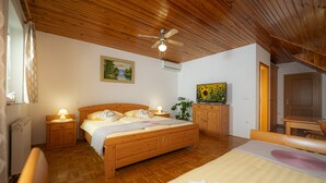 A bedroom with a wooden bed, bedside tables with lamps, a ceiling fan, a painting on the wall, and a television on a stand. - Rooms & Apartments Pr Matjon (Bled)