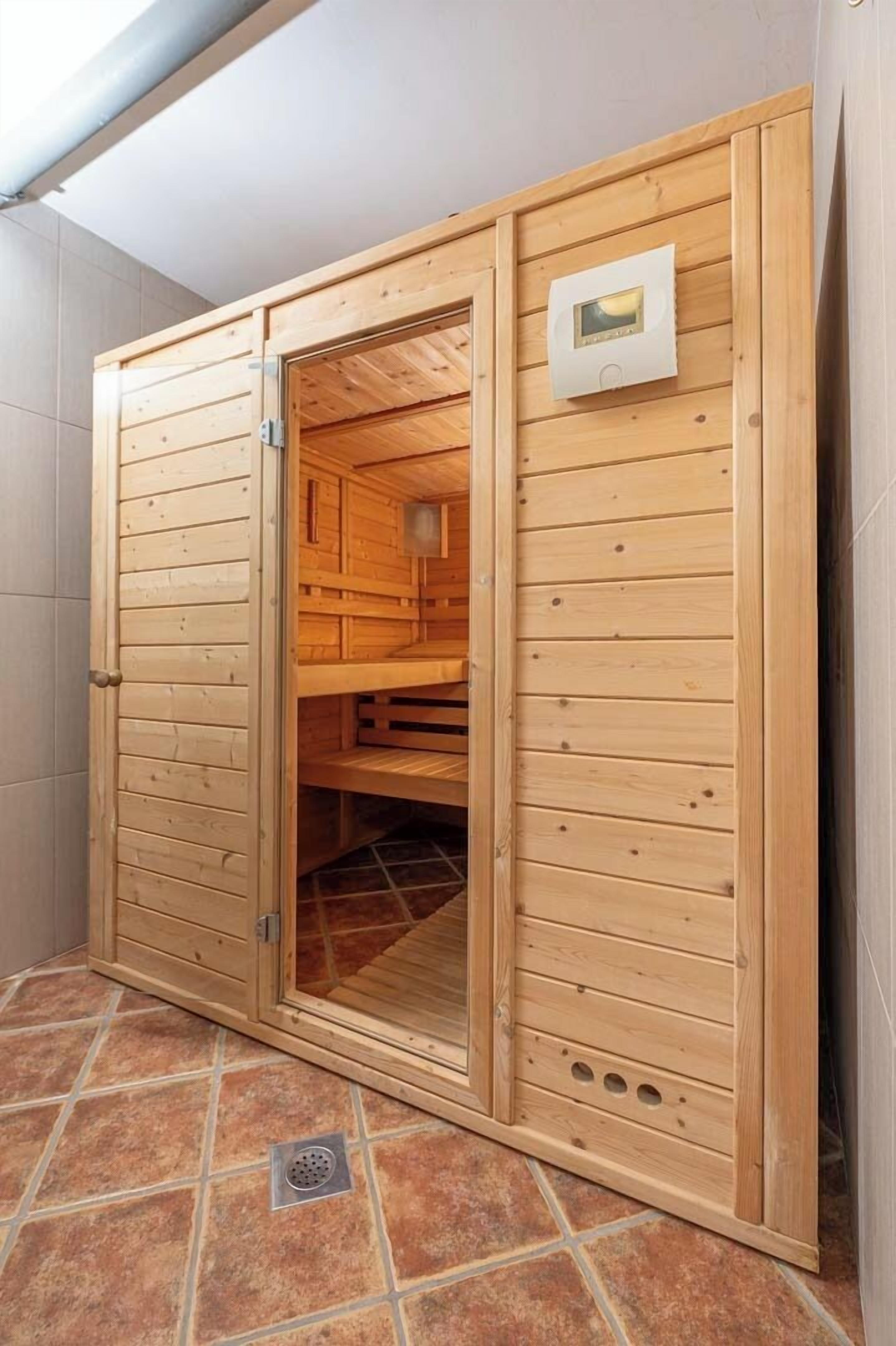 Un sauna en bois doté d’une porte coulissante, d’un panneau de commande fixé au mur et d’un sol carrelé.