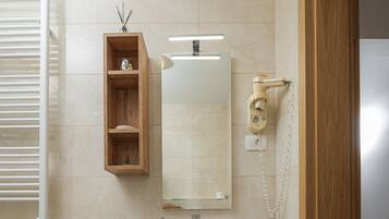 A bathroom with a white sink, a mirror, a wooden shelf with toiletries, a toilet paper holder, and patterned floor tiles.