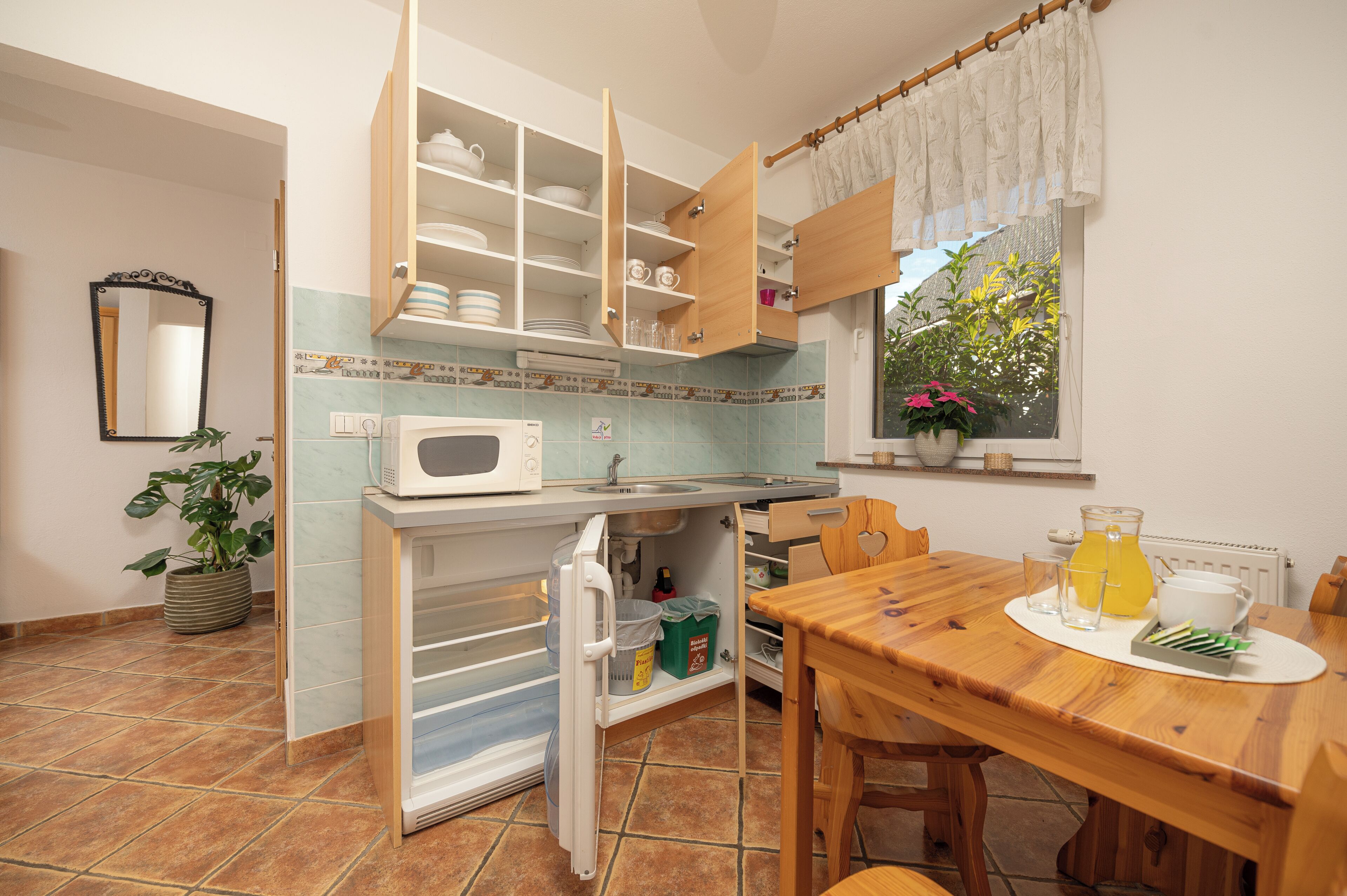 A compact kitchen with a refrigerator, microwave, and a dining table with a pitcher of juice.
