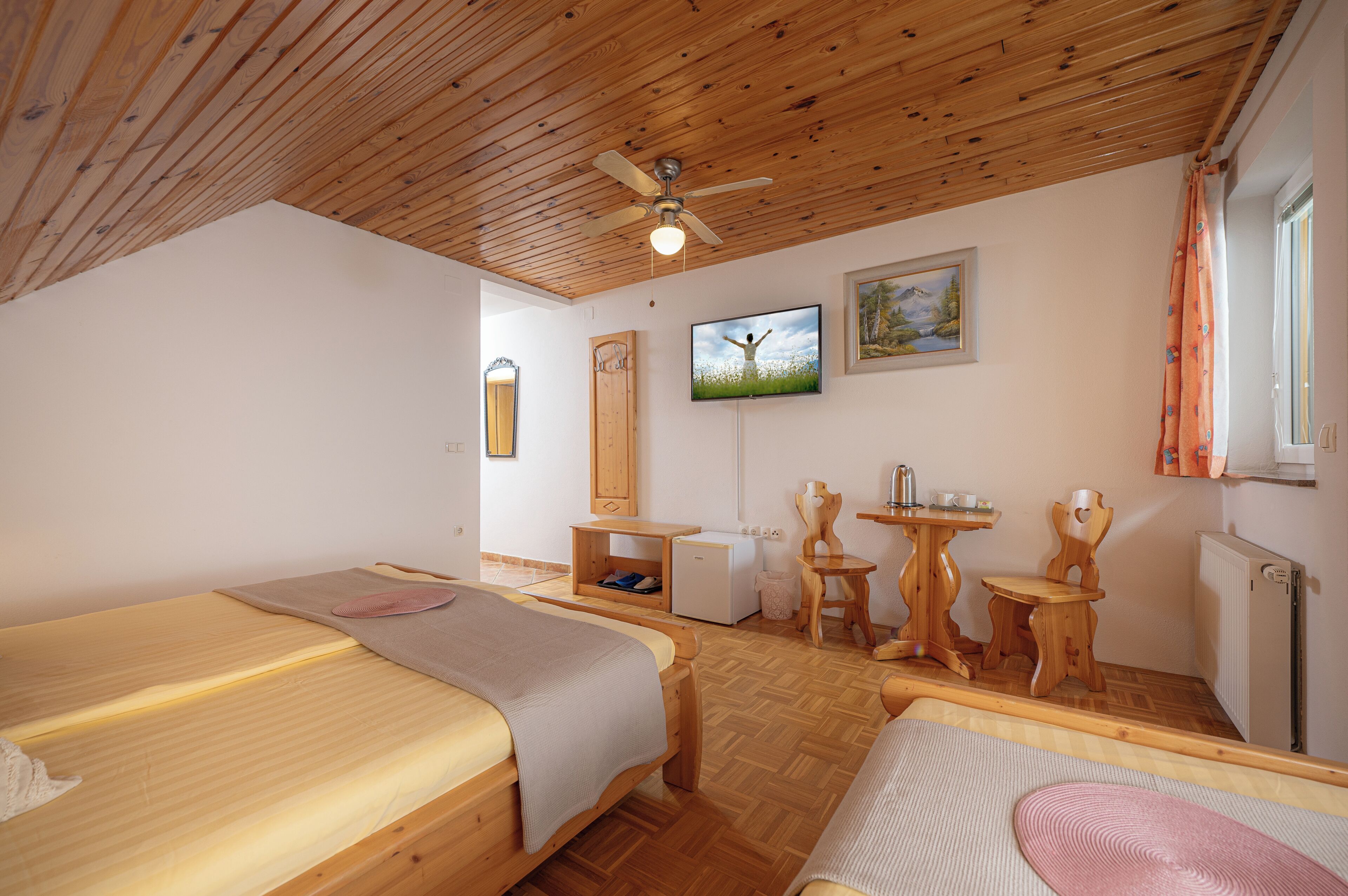A room with two beds, a ceiling fan, a TV, a small table, and a chair.