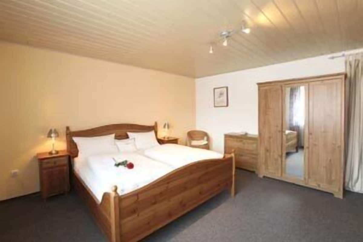 A wooden bed with white linens, a nightstand with a lamp, and a wooden wardrobe.