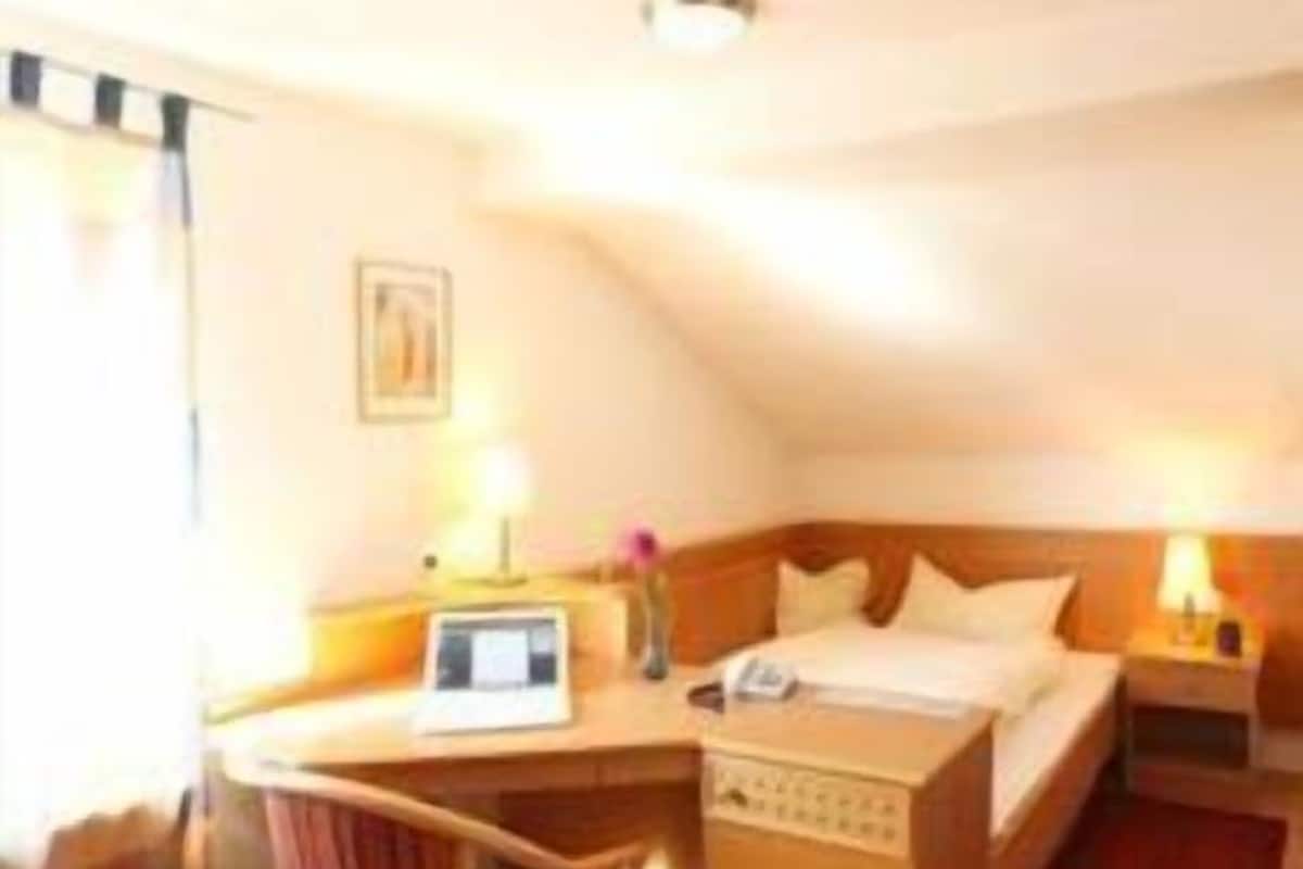 A hotel room with a bed, a desk, a chair, a nightstand, and a lamp.