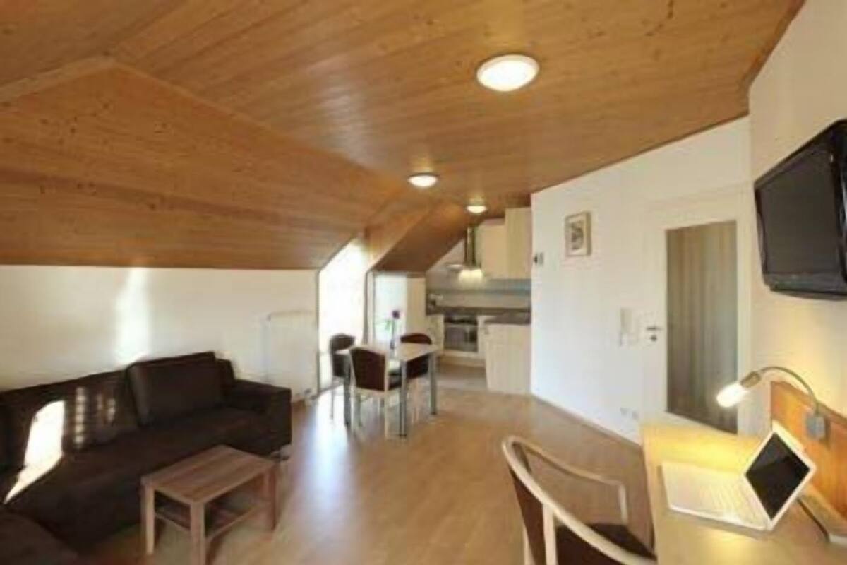 A modern living space with a wooden ceiling, a sofa, a dining table, and a laptop on a desk.