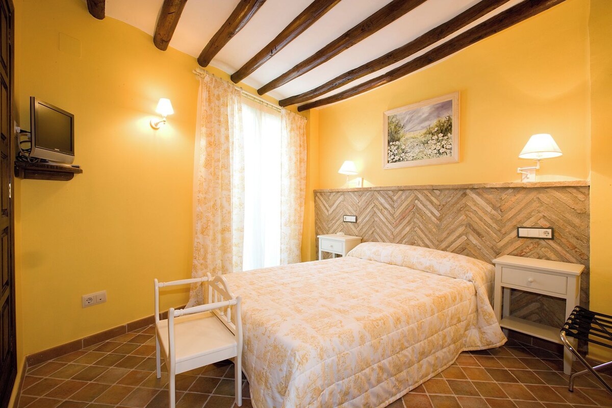 A bedroom with a bed, two bedside tables, a nightstand, a chair, a TV, and a painting on the wall.
