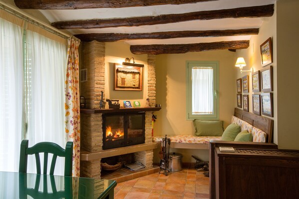 Una habitación acogedora con una chimenea de piedra, una cama con almohadas verdes y una mesa de comedor con sillas.
