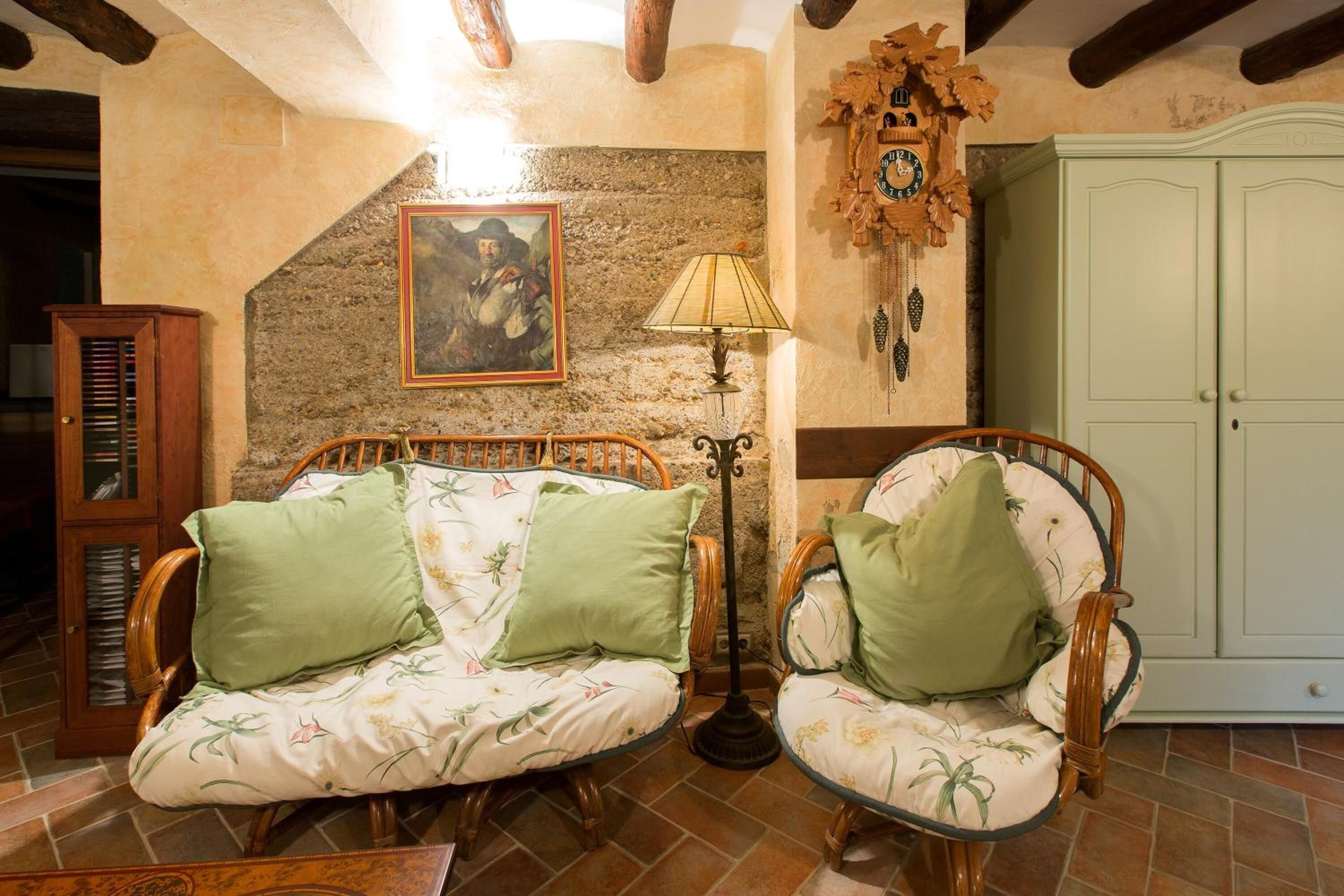 Una habitación acogedora con un sofá y sillones de madera, una lámpara, un reloj y un aparador.