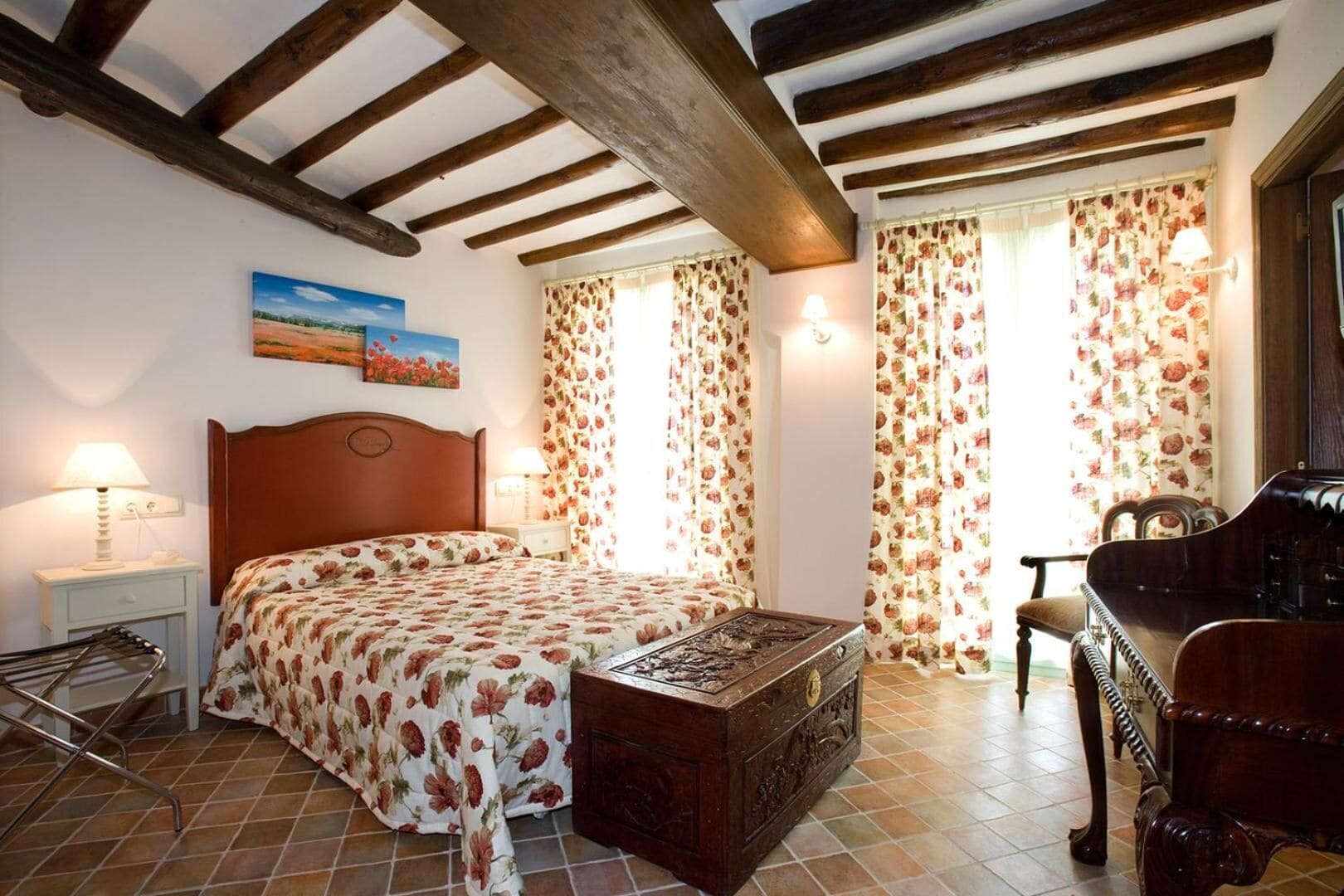 Un dormitorio con una cama de madera, una mesita de noche, una lámpara, un aparador, una silla y una ventana con cortinas florales.